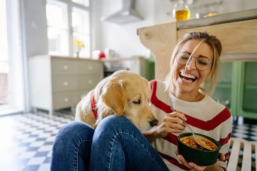 A woman with a bowl of food is playing with dog